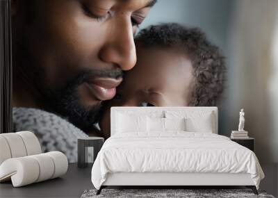 A man is holding a sleeping baby in his arms. The baby is wearing a blue sweater. The man's face is smiling, and the baby is looking up at him. Concept of warmth and love between the man Wall mural