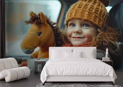 Child in a car seat, gazing out the window while holding a plush horse. Wall mural