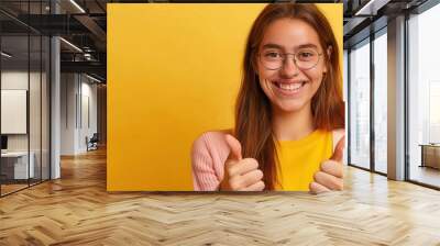 Smiling young woman in jacket, giving thumbs up. Free copy space for banner. Wall mural