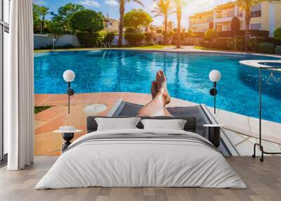 Relaxing at the swimming pool. Man relaxing next to swimming pool. Man enjoying the hot summer at swimming-pool. Sunbathing by the swimming pool, mans legs lying down on a sun lounger over the water. Wall mural