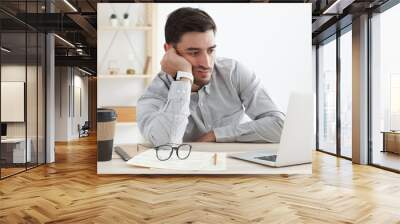 Business man in his office working on laptop, resting head on hand because he is tired, doing work overtime, stressed and bored Wall mural