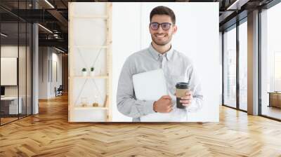 Caucasian guy standing in office pressing laptop to his chest and holding coffee cup, dreaming about future Wall mural