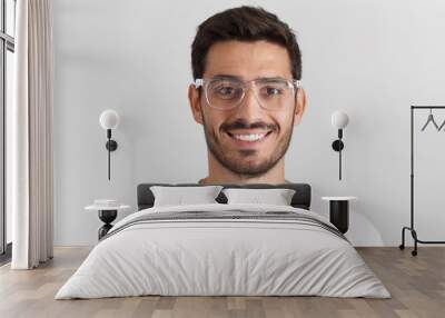 Close up daylight shot of smiling bearded man in white t-shirt and trendy trasparent eyeglasses, isolated on gray background Wall mural