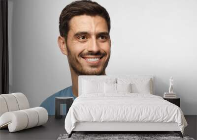 Close up portrait of smiling handsome male in blue t-shirt looking right, isolated on gray background Wall mural