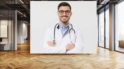 Close-up portrait of smiling handsome young male doctor with stethoscope around neck, wearing white coat and eyeglasses, isolated on gray background Wall mural