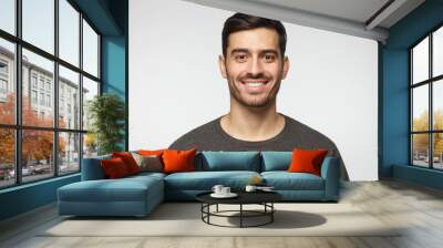 Close-up portrait of smiling handsome young man in casual t-shirt, isolated on gray background Wall mural