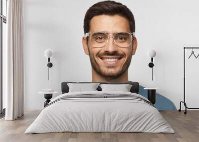 Close up shot of smiling attractive man in blue t-shirt and trendy trasparent eyeglasses isolated on gray background Wall mural