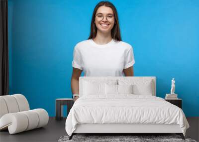 Closeup of positive European female dressed in white top isolated on blue background Wall mural