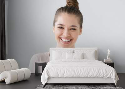 Closeup of positive teenage girl with brown hair tied in bun isolated on gray background with expression of happiness on face, laughing emotionally with excitement as if reacting to funny joke. Wall mural