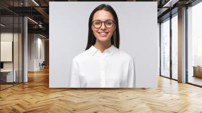 Closeup of young business lady wearing big eyeglasses and white collar shirt, smiling happily, ooking straight at camera, isolated on gray background Wall mural