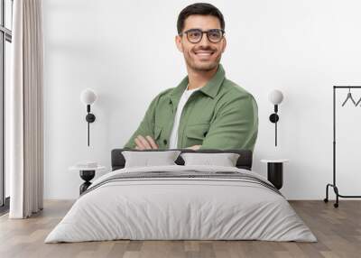 Confident young man in casual green shirt looking away, standing with crossed arms isolated on gray Wall mural