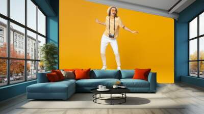 Dream about travel concept. Young funny female tourist standing on suitcase, pretending like she is surfing, isolated on yellow background Wall mural