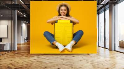 Excited young woman tourist sitting with large suitcase, isolated on yellow background Wall mural