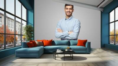 Handsome business man in blue shirt standing with crossed arms on gray background Wall mural