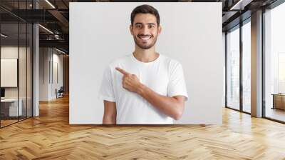 Handsome man in white t-shirt pointing left with finger isolated on gray background Wall mural