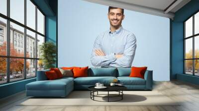 Handsome smiling business man in blue shirt standing with crossed arms on blue background Wall mural