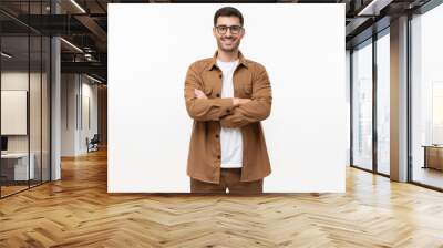 Handsome young man in brown workwear shirt and glasses, feeling confident with arms crossed, standing isolated on gray background Wall mural