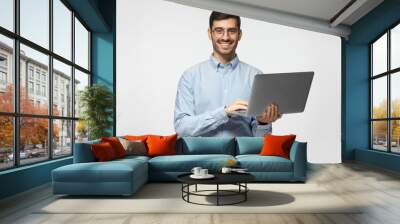 Handsome young man using laptop and looking at camera with smile, isolated on gray background Wall mural