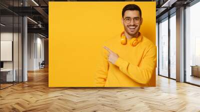 Horizontal banner of trendy man looking amazed and surprised pointing to copy space on left with finger, isolated on yellow background Wall mural