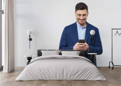 Horizontal banner of young man in glasses, blue blazer and shirt, smiling at content on his smart phone screen, copy space on left, isolated on gray background Wall mural