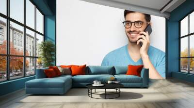 Horizontal banner of young smiling man in blue t-shirt holding phone in hand and looking away, isolated on gray background Wall mural