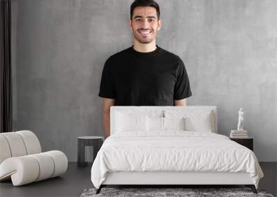 Hotizontal portrait of young man wearing blank black t-shirt and jeans, posing against gray textured wall Wall mural