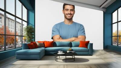 Indoor portrait of young european caucasian man isolated on gray background, standing in blue t-shirt with  crossed arms, smiling and  looking straight at camera Wall mural