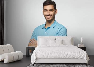 Portrait of attractive young sporty man in blue polo shirt standing with crossed arms, isolated on gray background Wall mural