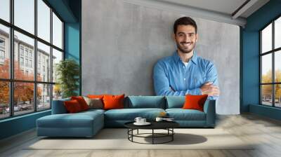 Portrait of smiling handsome man in blue shirt standing with crossed arms against gray textured wall with copy space Wall mural