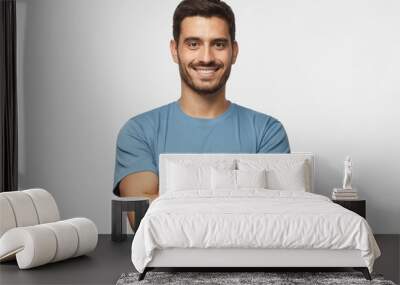 Portrait of smiling handsome man in blue t-shirt standing with crossed arms isolated on grey background Wall mural