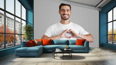 Portrait of smiling young man keeps hands on chest in heart shape sign Wall mural