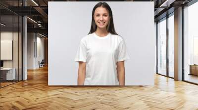 Portrait of smiling young woman in white t-shirt looking at camera, isolated on gray background Wall mural