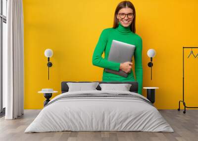 Portrait of woman secretary holding closed laptop on yellow background with copy space Wall mural