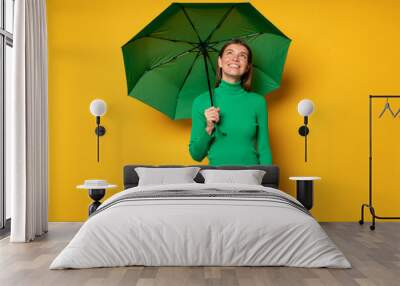 Portrait of woman standing under green umbrella on yellow background enjoying rainy day Wall mural