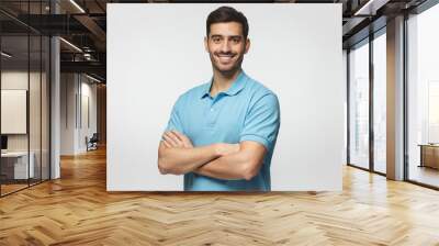 Portrait of young european caucasian man isolated on gray background, standing in blue polo shirt with crossed arms, smiling and  looking at camera Wall mural