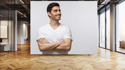 Portrait of young man with crossed arms and dreamy cheerful expression, thinking, isolated on gray background with copy space Wall mural