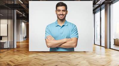 Smiling handsome man in blue polo shirt standing with crossed arms isolated on gray background Wall mural