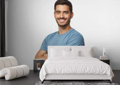 Smiling handsome young man in blue t-shirt standing with crossed arms, isolated on grey background Wall mural