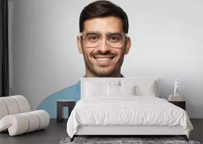 Smiling modern nice guy in blue polo shirt and trendy trasparent eyeglasses, isolated on gray background Wall mural