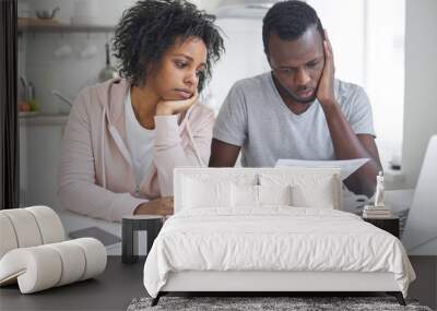 Stressed african american couple looking frustrated, having no money to pay off their debts, managing family budget together, sitting home at kitchen table with lots of papers, laptop and calculator Wall mural