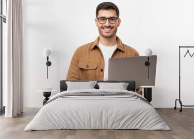 Studio portrait of young man standing holding laptop and looking at camera with happy smile, isolated on gray Wall mural