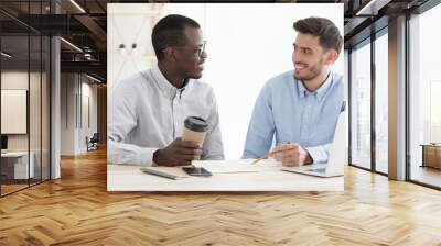 Two male mixed race colleagues sitting at office desk, checking data in documents of their common multiethnic project Wall mural