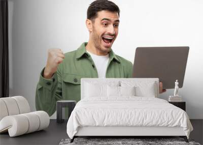 We got a winner! Excited young man in green shirt looking at laptop screen with WOW expression, isolated on gray background Wall mural