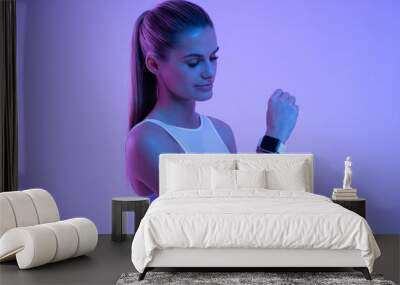 Woman adjusting settings of fitness tracker before start of training session in neon light Wall mural