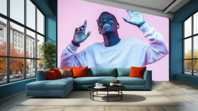 Young african man listening to music with wireless earphones and dancing isolated on pink background Wall mural