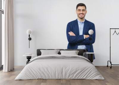 Young business man standing in front of camera with arms crossed, looking at camera through glasses with positive friendly smile, isolated on gray background with copy space Wall mural