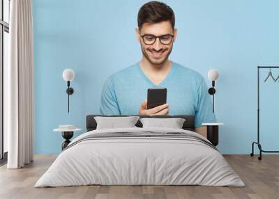 Young handsome man in blue t-shirt holding smartphone and looking at phone screen Wall mural