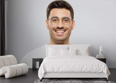 Young handsome smiling man dressed in white casual t-shirt and wearing glasses, feeling confident at work, isolated on gray background Wall mural