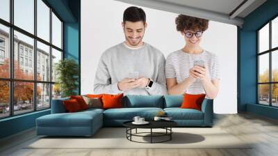 Young happy couple holding smartphones and standing shoulder to shoulder isolated on gray background Wall mural