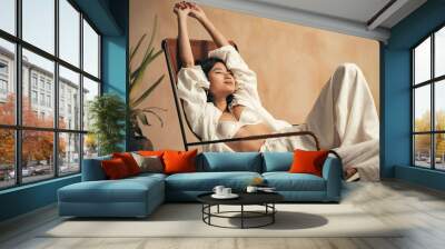 Young korean model relaxing on lounger on background with brown textured wall, stretching hands Wall mural